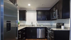 Une cuisine moderne avec des meubles de couleur sombre, des appareils électroménagers en acier inoxydable et un plan de travail en granit.