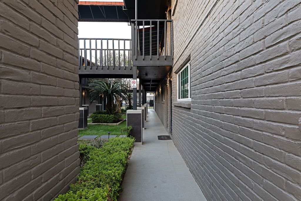 A narrow alleyway with brick walls, a concrete pathway, and a small garden area with greenery.