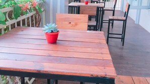 Eine Terrasse im Freien mit Holztischen und -stühlen, Blumentöpfen und einem weißen Geländer.