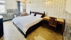Ein Schlafzimmer mit Bett, Nachttischen, einem Sessel, einem Schreibtisch und einem Fenster mit Vorhängen.