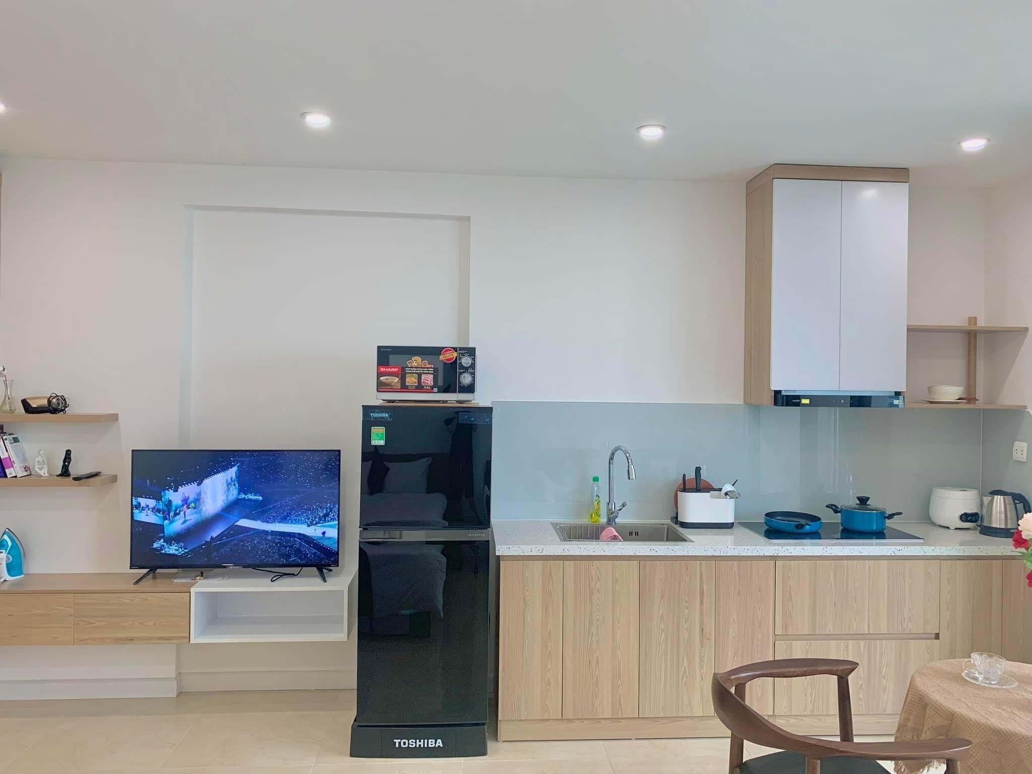 Una cocina moderna con refrigerador integrado, televisor de pantalla plana y un comedor con mesa y sillas de madera.
