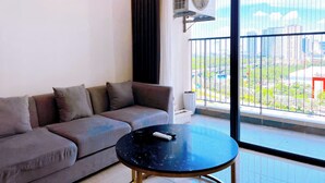 A modern living room with a grey sofa, a round black coffee table, and a large window with a view of a cityscape. - Vinhomes D'Capitale Residence - CitiHome (Hanoi)
