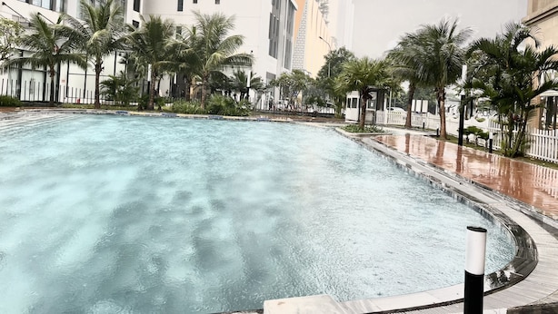 A swimming pool with a curved edge, surrounded by palm trees and a white fence. - Vinhomes D'Capitale Residence - CitiHome (Hanoi)
