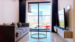 A modern living room with a sofa, a glass-top coffee table, a flat-screen TV, and a large window with a view of buildings. - Vinhomes D'Capitale Residence - CitiHome (Hanoi)