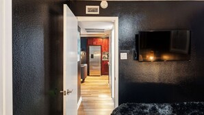 A hallway with a black wall, a mounted TV, and a door leading to a kitchen area.