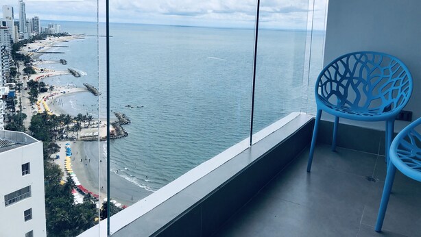 A balcony with a view of a beach and ocean, a blue chair, and a logo for 'Lamar'. - Murano Elite Piso 25 (Cartagena de Indias)