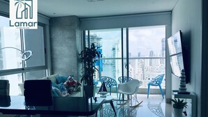 A modern living room with a large window, a sofa, a coffee table, and a TV. - Murano Elite Piso 25 (Cartagena de Indias)