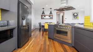 A modern kitchen with a stainless steel refrigerator, built-in oven, and a dining area with a yellow accent wall. - Jindy Snowy Mountains Retreat (Jindabyne)