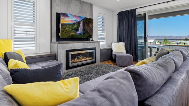 A modern living room with a fireplace, grey sofas, yellow cushions, and a large TV mounted above the fireplace. - Jindy Snowy Mountains Retreat (Jindabyne)