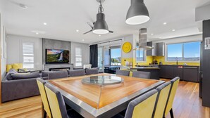 A modern living room with a wooden dining table, grey sofas, and a flat-screen TV. - Jindy Snowy Mountains Retreat (Jindabyne)