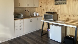 A compact kitchen with wooden cabinetry, a microwave, a toaster, and a small refrigerator.
