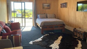 A bedroom with a bed, a sofa, a rug, and a window with a view of the outdoors.