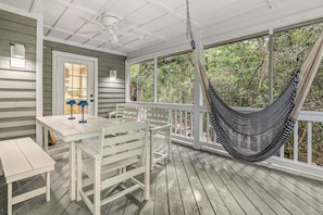 A porch with a white table and chairs, a hammock, and a view of the surrounding greenery.