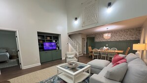 A living room with a television, a sofa, a coffee table, a dining area with chairs, and a staircase.