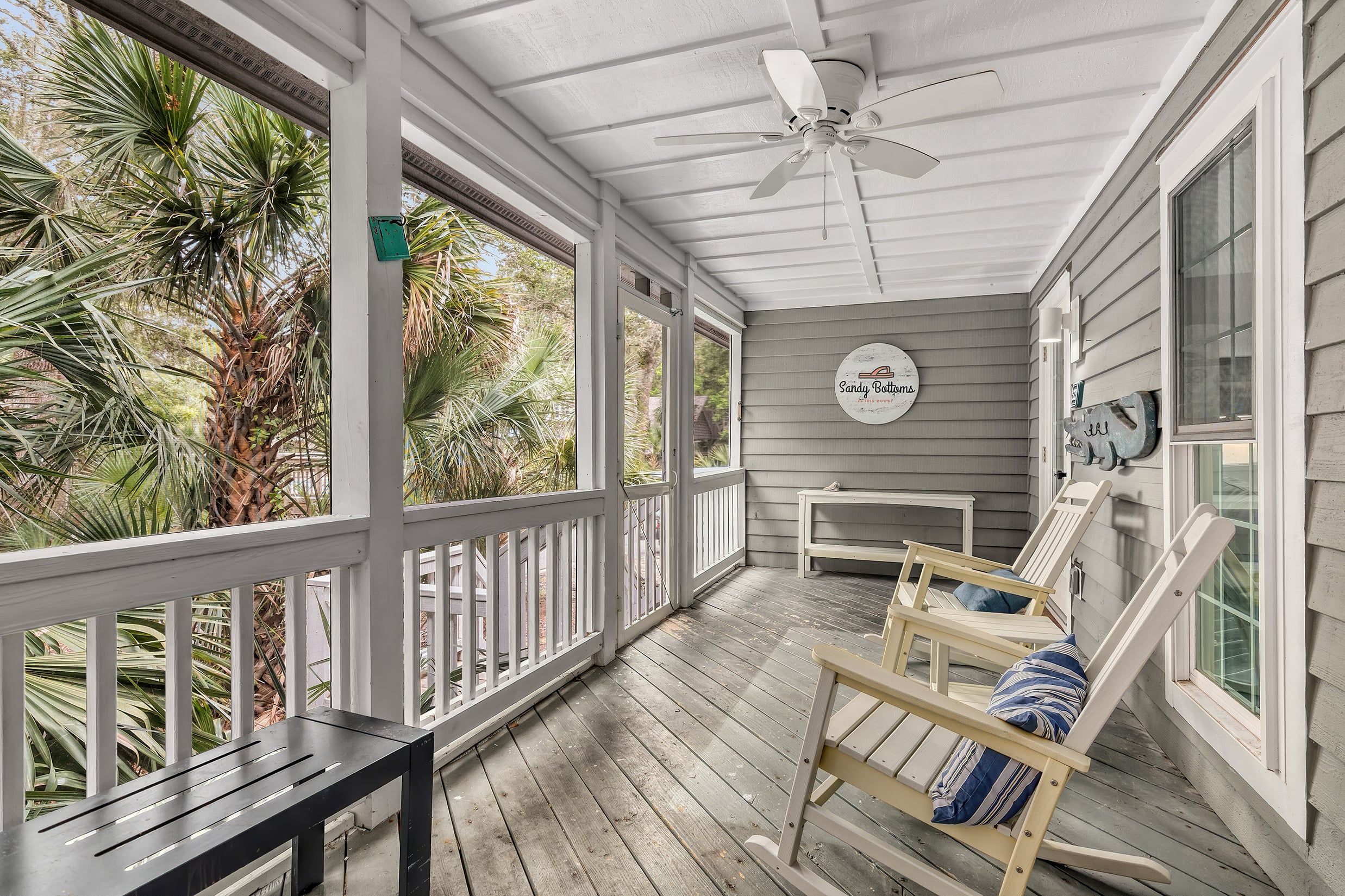A covered porch with a ceiling fan, wooden railing, and a bench with cushions.