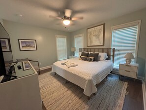 Quarto com cama, ventilador de teto, mesa de cabeceira, luminária e obras de arte emolduradas nas paredes.