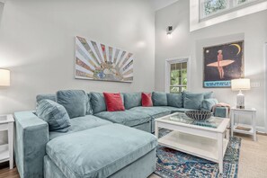 Una sala de estar moderna con un sofá seccional azul claro, una mesa de centro de vidrio y una alfombra estampada.
