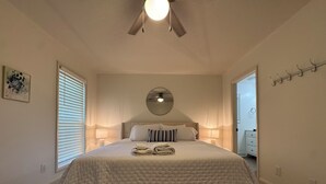 A bedroom with a bed, bedside lamps, a ceiling fan, and a door leading to another room.