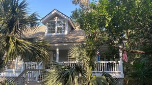 A house with a porch, surrounded by palm trees and a fence.