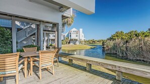 Une terrasse en bois, agréée de mobilier d’extérieur, qui offre une vue sur une étendue d’eau et une zone résidentielle.