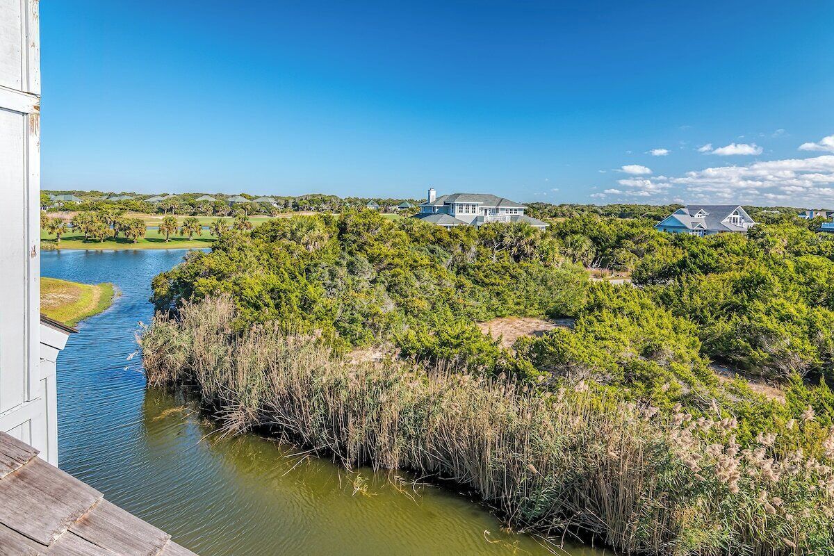 A riverside view with a wooden deck, dense greenery, and multiple houses.