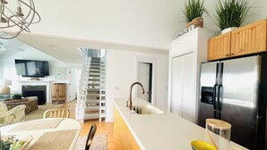 Une cuisine moderne dotée d’un îlot central, d’appareils électroménagers en acier inoxydable et d’un escalier menant à un étage supérieur.