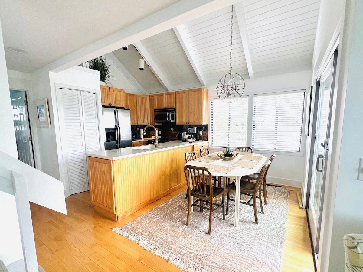 A modern kitchen with wooden cabinets, a central island, and a dining area with a table and chairs.