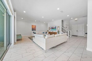 A spacious living room with a white sofa, a glass door, and a staircase leading to another level. - 10Br Spacious Villa With Private Oversized Pool, Close To Disney (Davenport)