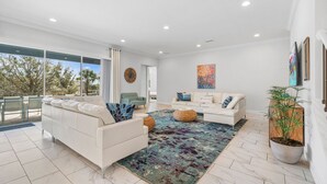 A modern living room with a white sofa, a patterned rug, and a large window offering a view of trees. - 10Br Spacious Villa With Private Oversized Pool, Close To Disney (Davenport)
