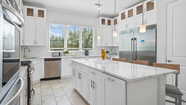 A modern kitchen with white cabinetry, a large island, stainless steel appliances, and a view of trees through the windows. - 10Br Spacious Villa With Private Oversized Pool, Close To Disney (Davenport)