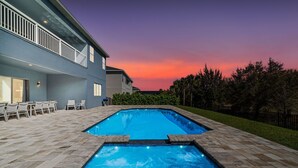 A rectangular swimming pool with a stone border, surrounded by a patio with chairs and a building with a balcony. - 10Br Spacious Villa With Private Oversized Pool, Close To Disney (Davenport)