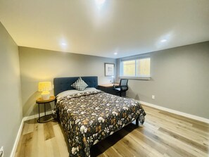 Une chambre à coucher avec un lit, un bureau, une chaise, une lampe et une fenêtre.