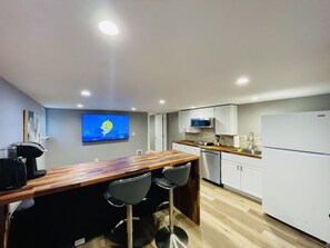Una cucina moderna con un bancone in legno, due sgabelli da bar, mobili bianchi, un frigorifero in acciaio inossidabile e un televisore a schermo piatto montato a parete.