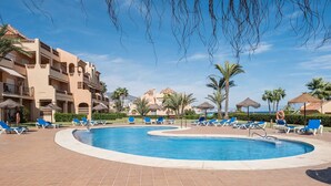 Zwembadgedeelte van een resort met meerdere ligbedden en een helder uitzicht op de oceaan op de achtergrond.