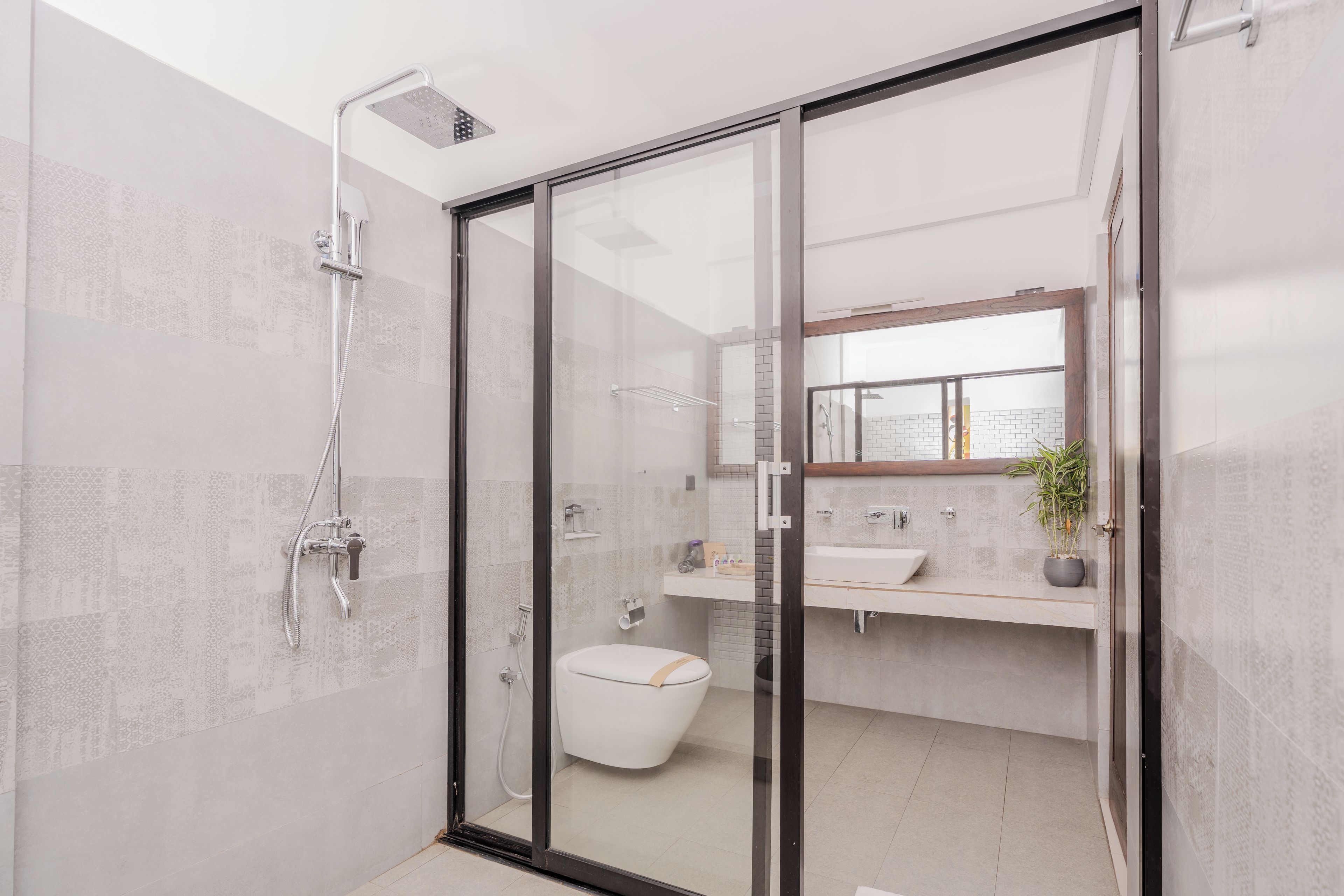 A modern bathroom with a glass shower enclosure, a toilet, and a sink with a mirror above.