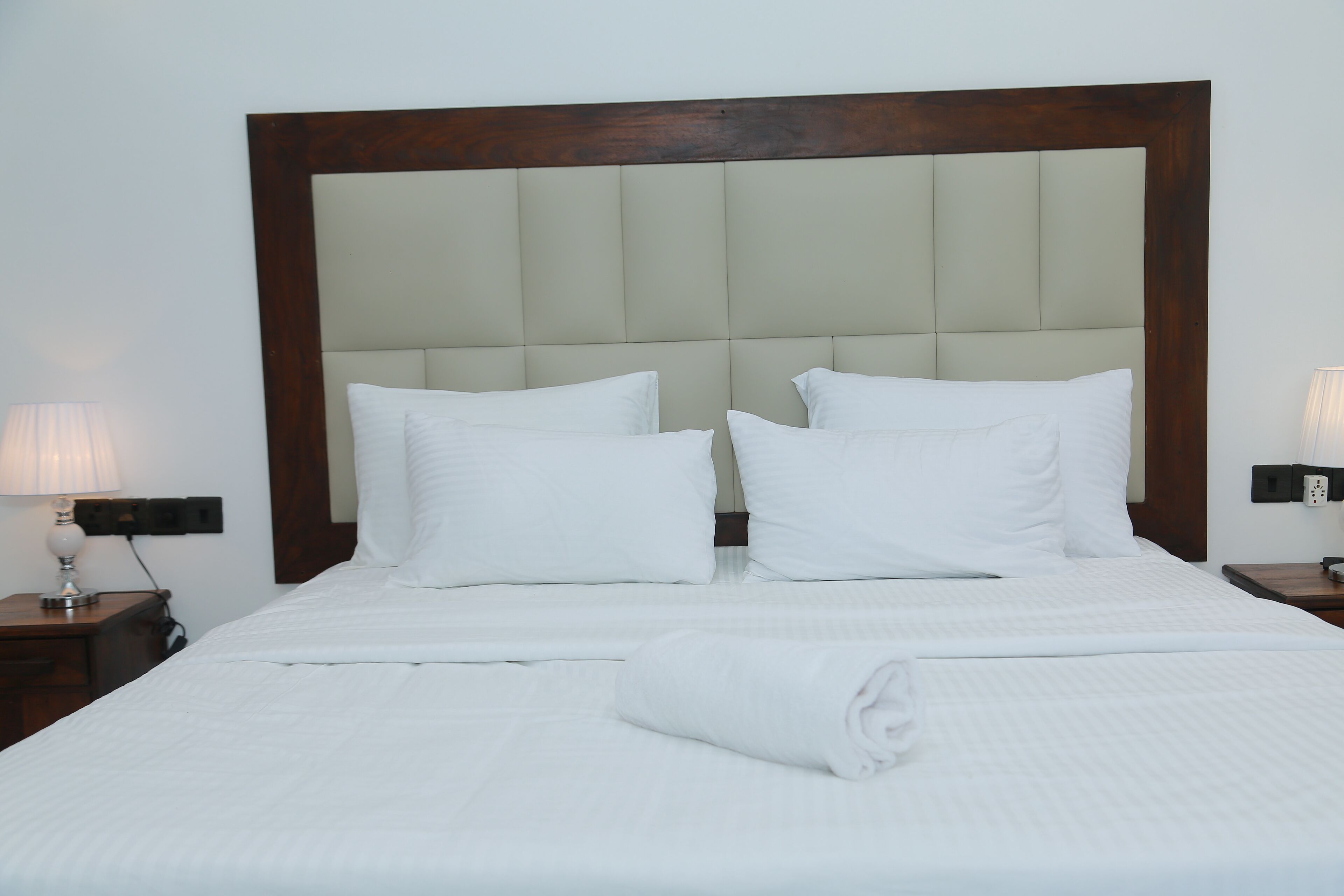 A neatly made bed with a wooden headboard, white bedding, and two bedside lamps.