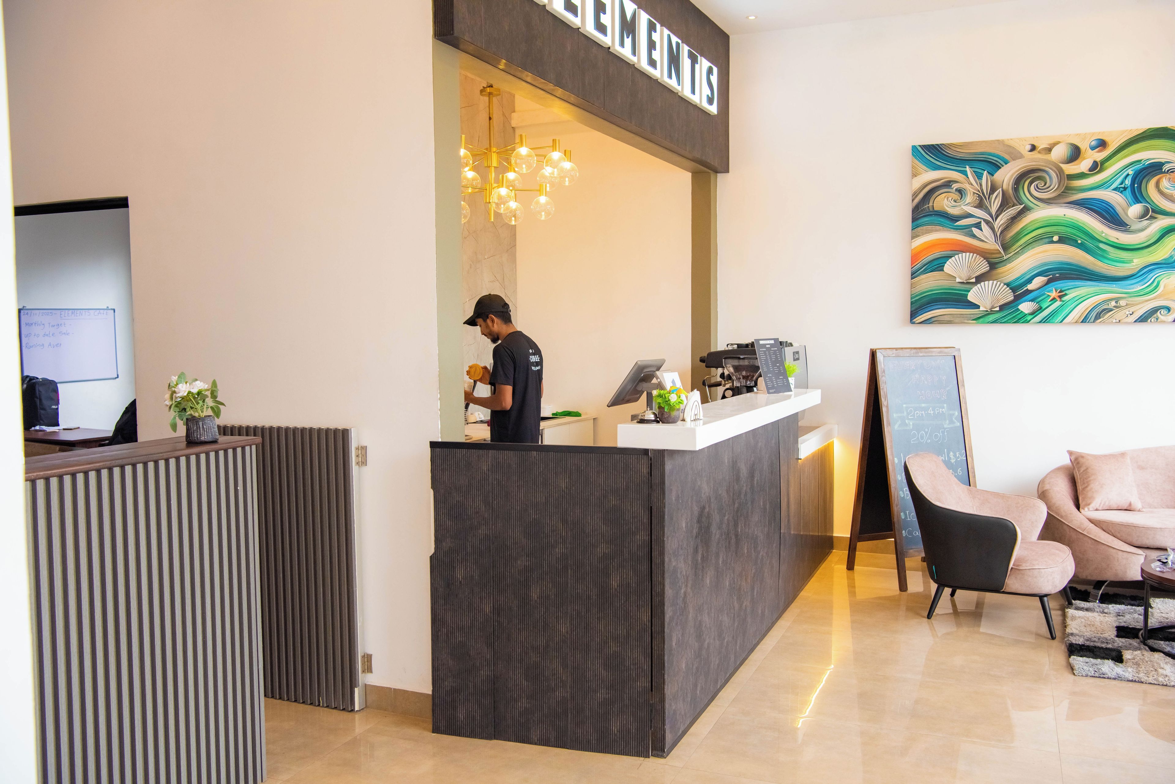 Un comptoir d’accueil avec une enseigne au-dessus, un distributeur de café, un tableau noir indiquant une promotion, une plante et un tableau accroché au mur.