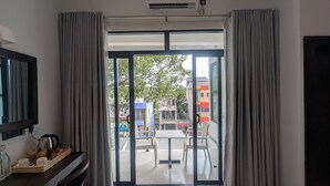 A modern hotel room with a large sliding glass door leading to a balcony, a flat-screen TV, and a small table with a kettle and cups. - Mzion Hotel Weligama (Weligama)