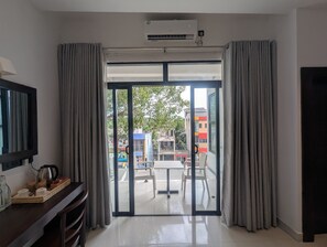 Een moderne hotelkamer met een grote schuifglazen deur naar een balkon, een flatscreen televisie en een klein tafeltje met waterkoker en kopjes.