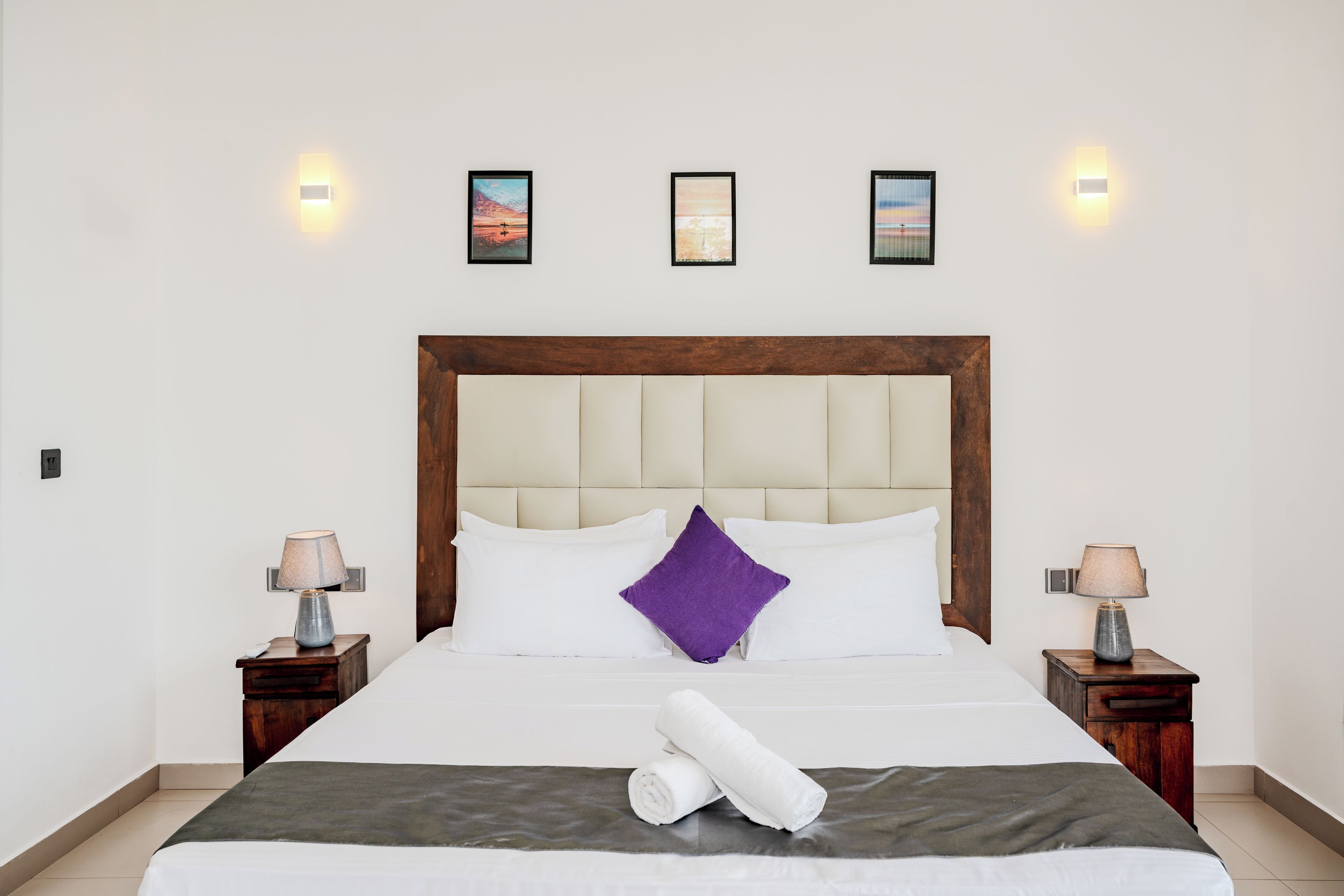 A hotel room with a large bed, two bedside tables with lamps, and three framed pictures on the wall.
