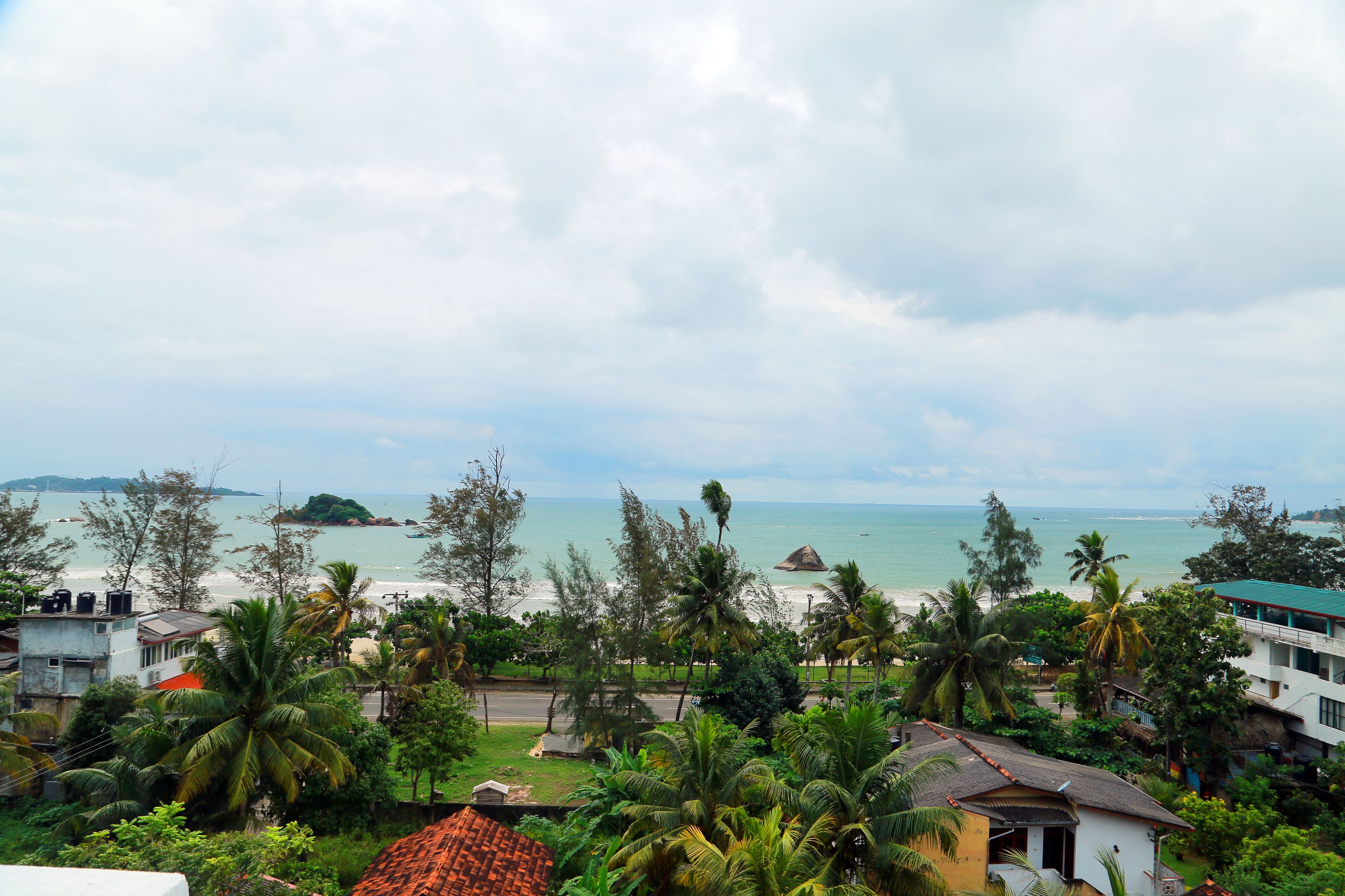 A coastal view with a beach, palm trees, and buildings.