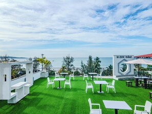 Un espace extérieur aménagé avec des tables et des chaises blanches, une vue sur la mer et une enseigne indiquant « M-ZION ».