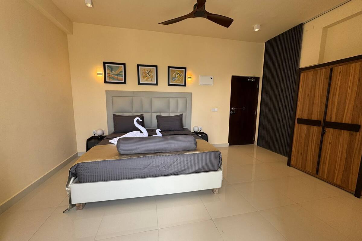 A bedroom with a bed, a ceiling fan, a door, and framed artwork on the wall.