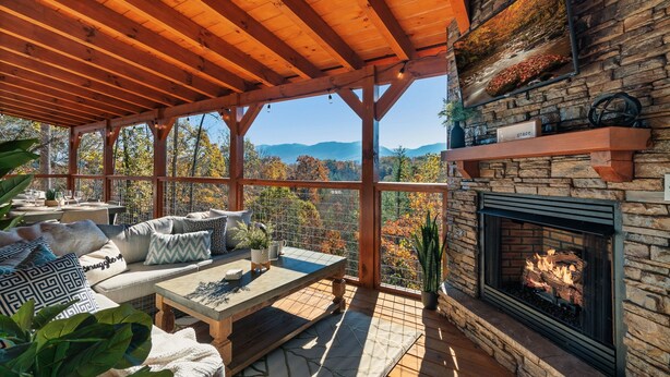 A covered outdoor seating area with a stone fireplace, wooden beams, and a view of the mountains.
