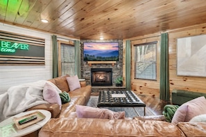 Ein gemütliches Blockhaus-Interieur mit Kamin aus Stein, Ledersofas und einem an der Wand befestigten Fernseher.