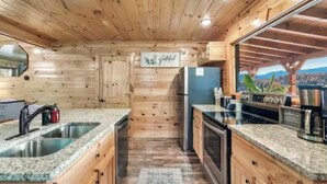 A wooden cabin interior with a kitchen featuring granite countertops, a refrigerator, and a coffee station.