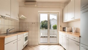 A compact kitchen with a sink, stove, and microwave. It features a sliding glass door leading to a balcony with a white railing.