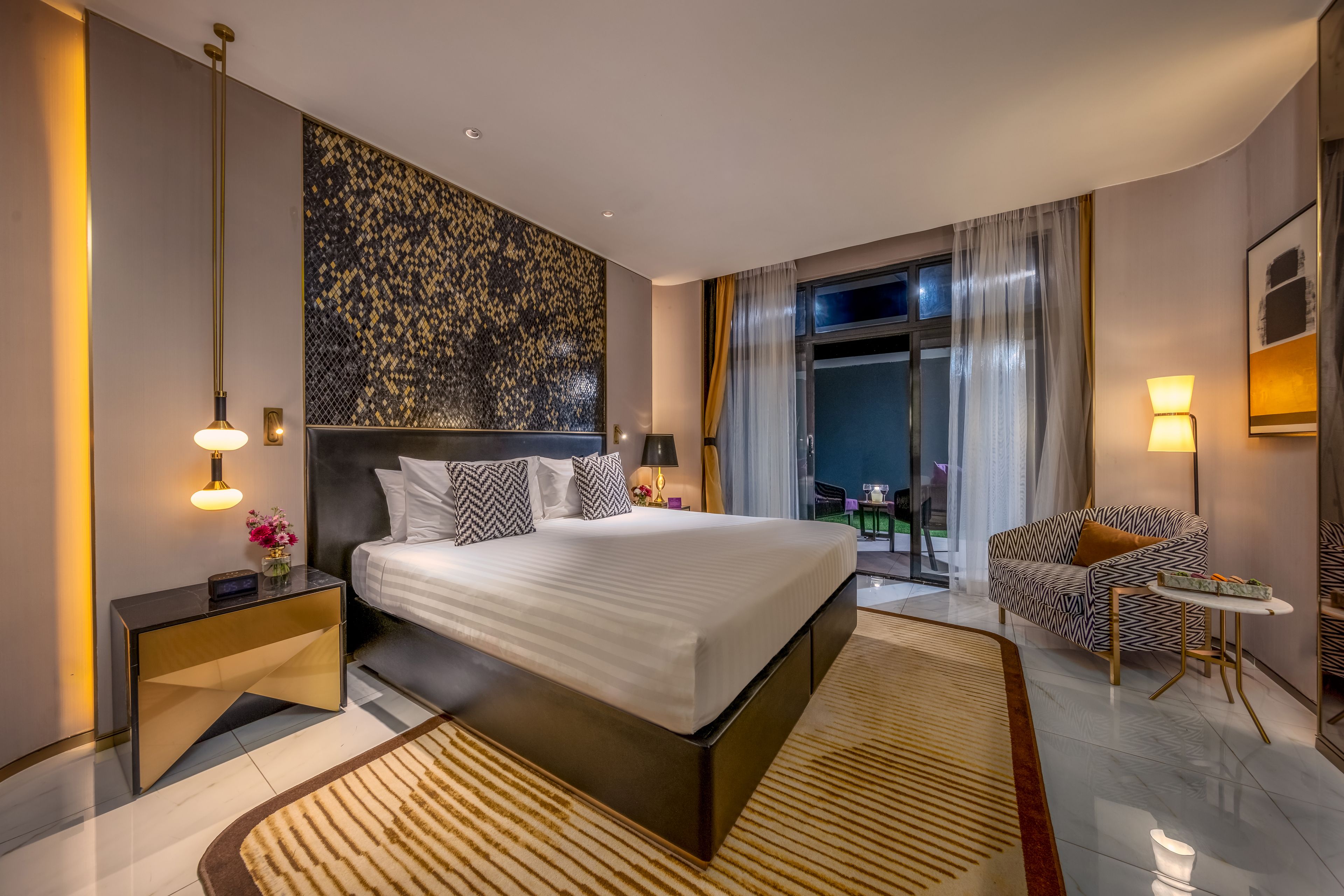 A modern hotel room with a large bed, a desk, a chair, and a view of the outdoors.