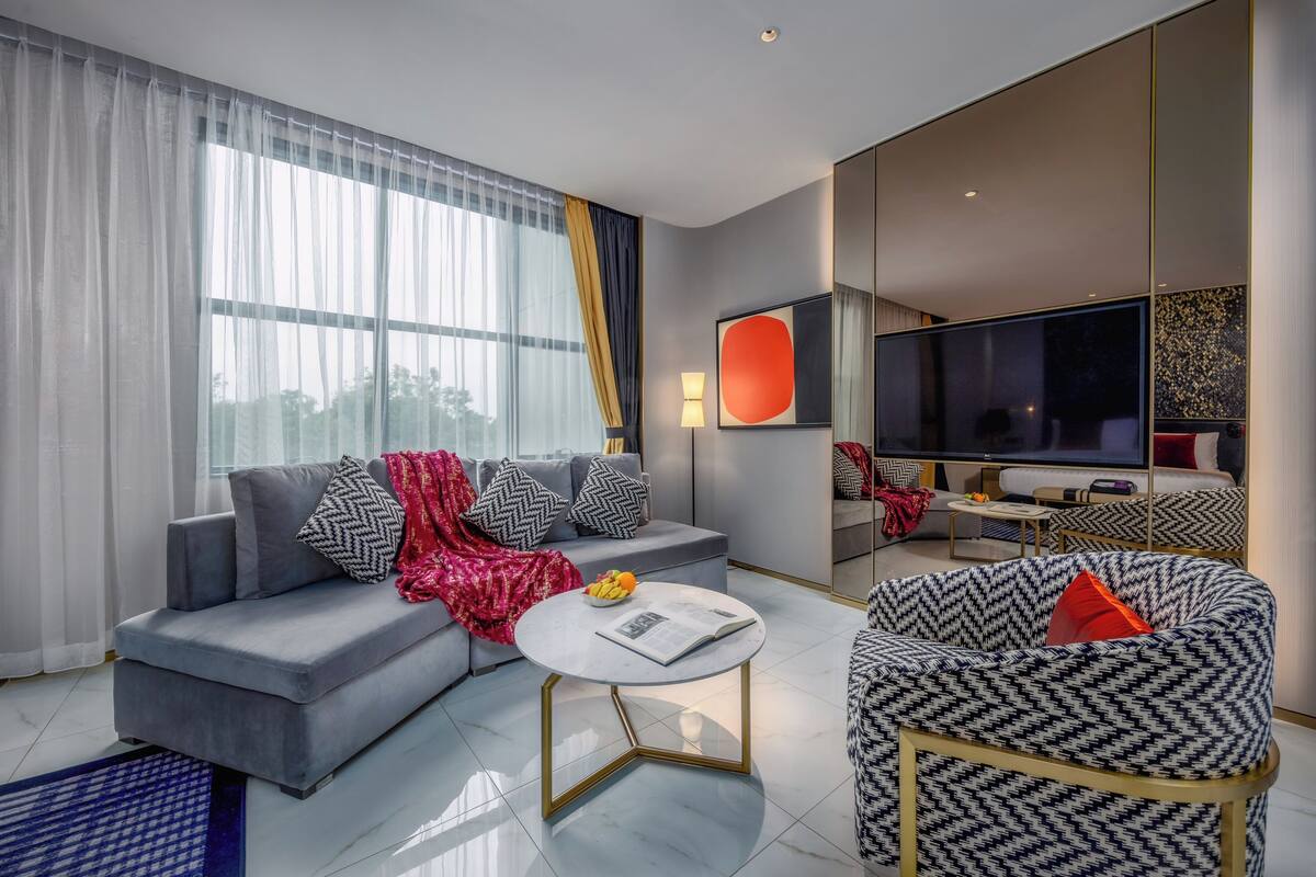 A modern living room with a grey sofa, a patterned armchair, a round coffee table, and a flat-screen TV.