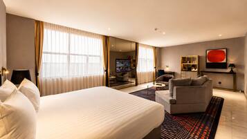 A hotel room with a large bed, a sofa, a TV, and a red abstract painting.